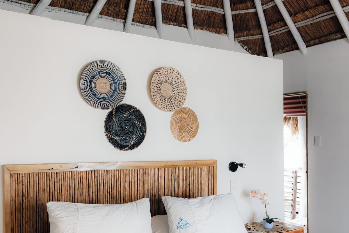 A bedroom with a thatched roof, a wooden headboard, and a bed with white bedding and a blue accent.