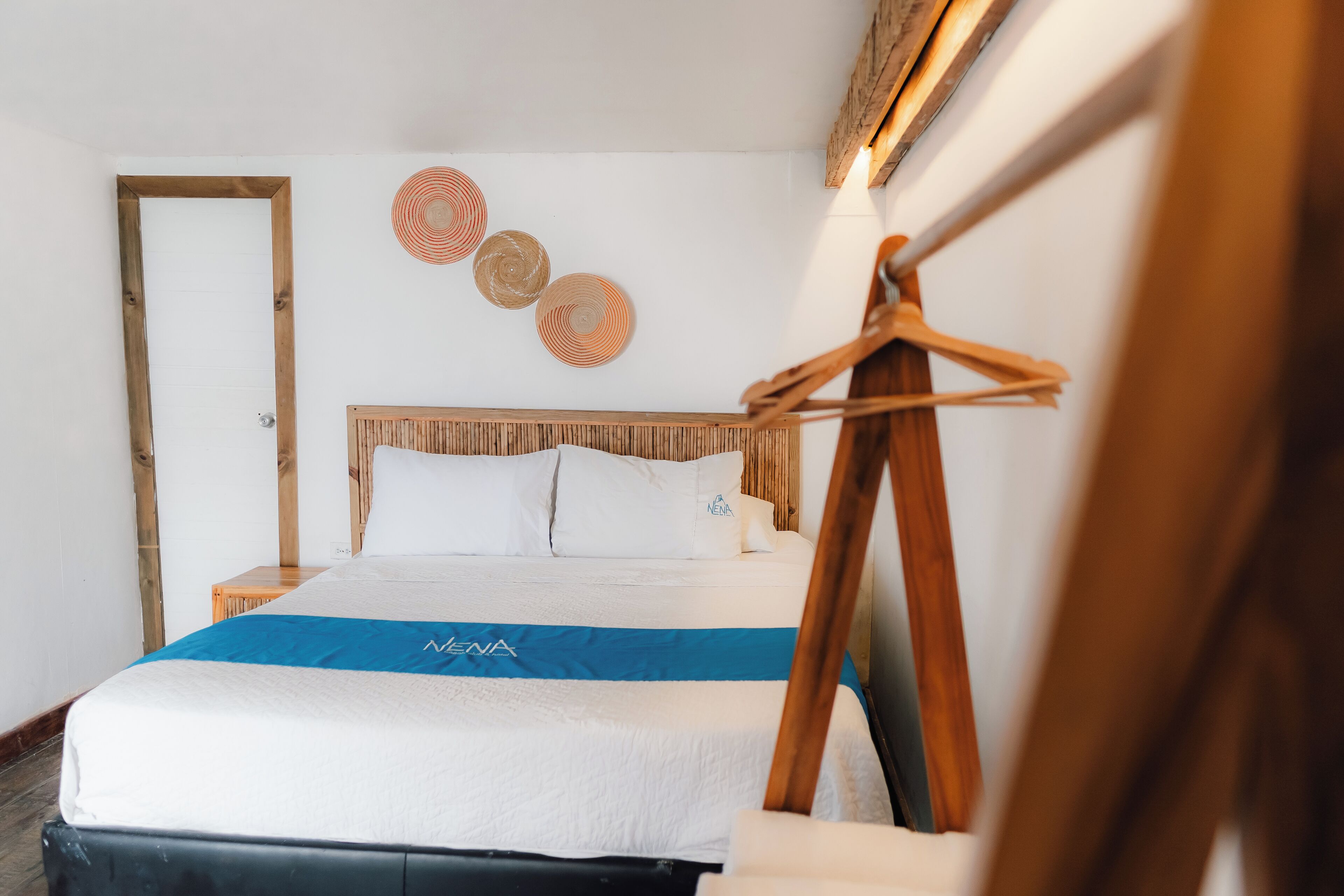 Una cama bien hecha con una colcha azul y blanca, un cabecero de madera y tres adornos circulares en la pared.