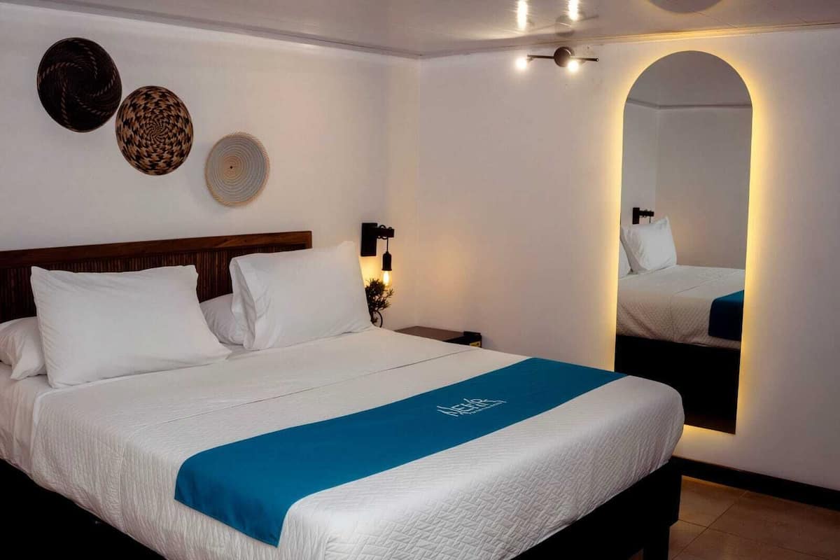 A hotel room with a large bed, a nightstand, a wall-mounted lamp, and decorative wall art.