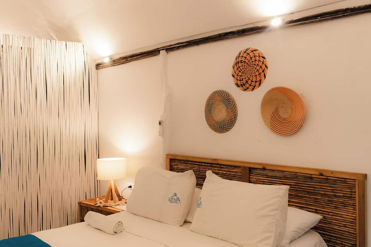 A neatly made bed with a blue bedspread, a wooden headboard, and a wall with three woven wall hangings.