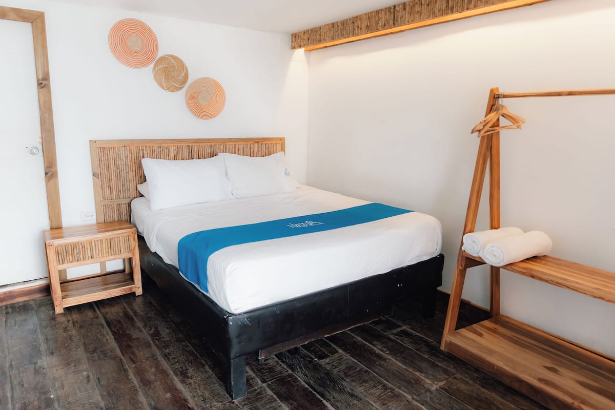 A neatly arranged hotel room with a bed, a wooden bedside table, a hanging clothes rack, and a small shelf.