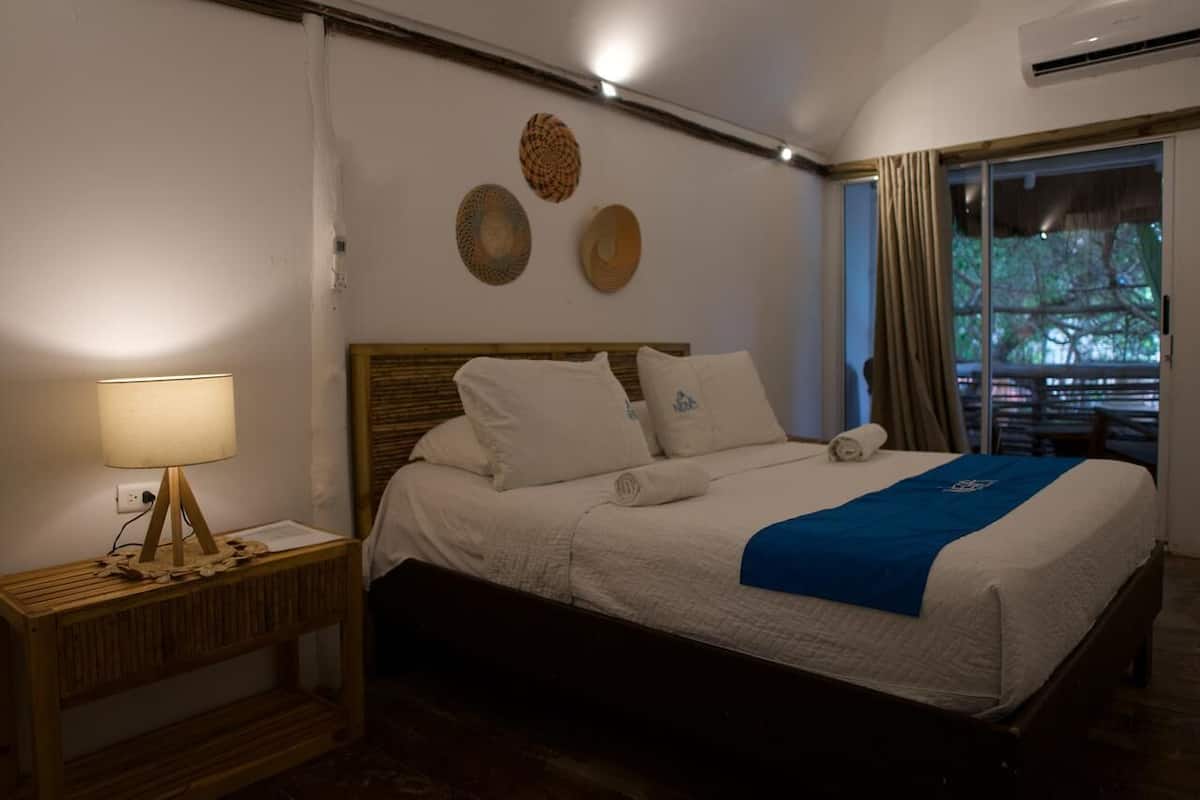 A neatly made bed with a blue blanket, a bedside lamp, and a wooden nightstand.