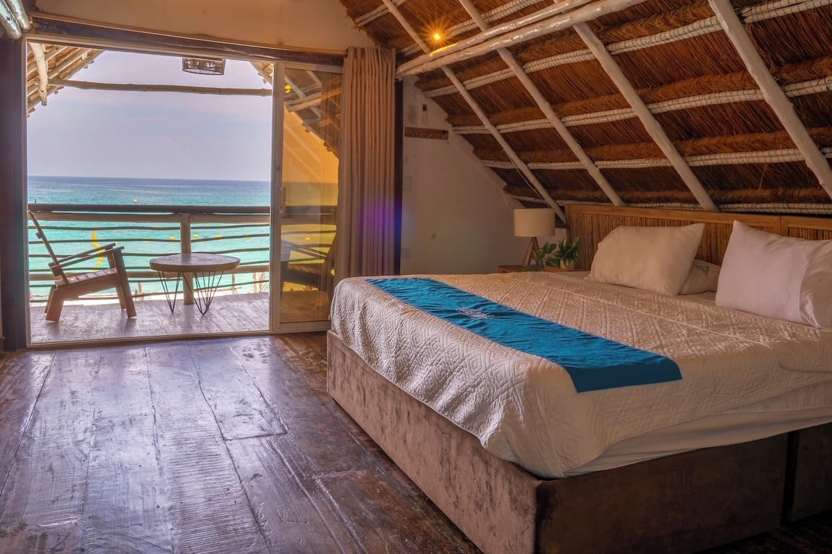 A room with a bed, a chair, a table, and a view of the ocean.