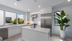 A modern kitchen with white cabinetry, a stainless steel refrigerator, and a large island with a sink. - Bleuphoria! Rooftop Views and Poolside Fun! (Anna Maria)