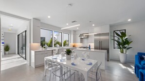 A modern kitchen with white cabinets, stainless steel appliances, and a central island with clear chairs. - Bleuphoria! Rooftop Views and Poolside Fun! (Anna Maria)
