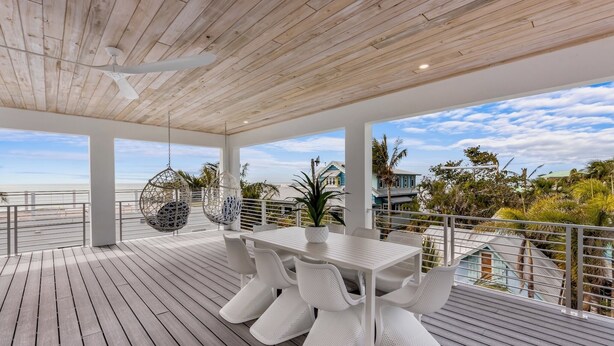 A covered outdoor deck with a white table and chairs, a hanging chair, and a potted plant. - Bleuphoria! Rooftop Views and Poolside Fun! (Anna Maria)