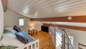 Ein Schlafzimmer im Loft-Stil mit Holzbalkendecke, einem Bett mit Kissen, einem kleinen Tisch mit Lampe und einer Treppe.