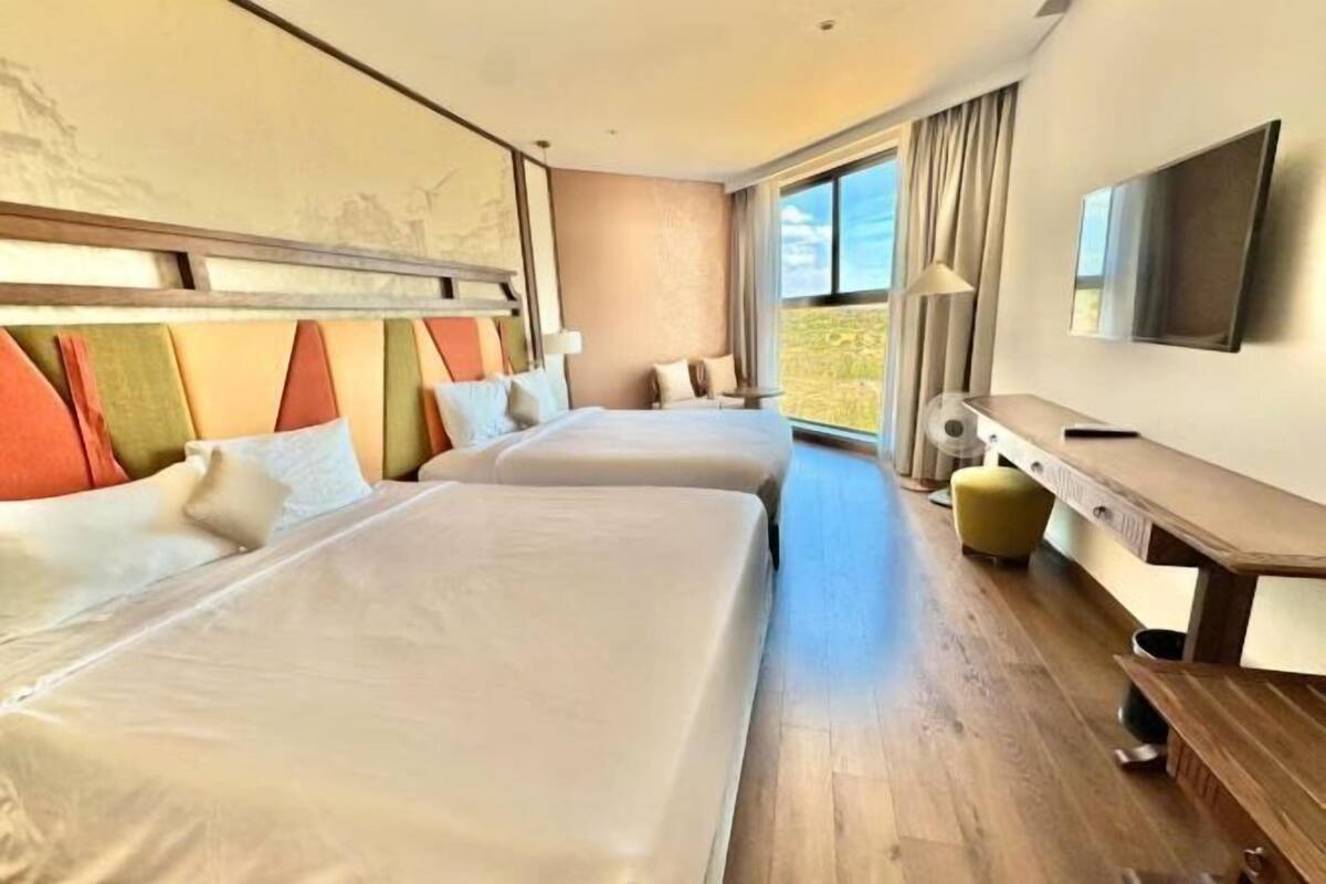 Une chambre d’hôtel avec deux lits, une télévision, un bureau et une grande fenêtre.