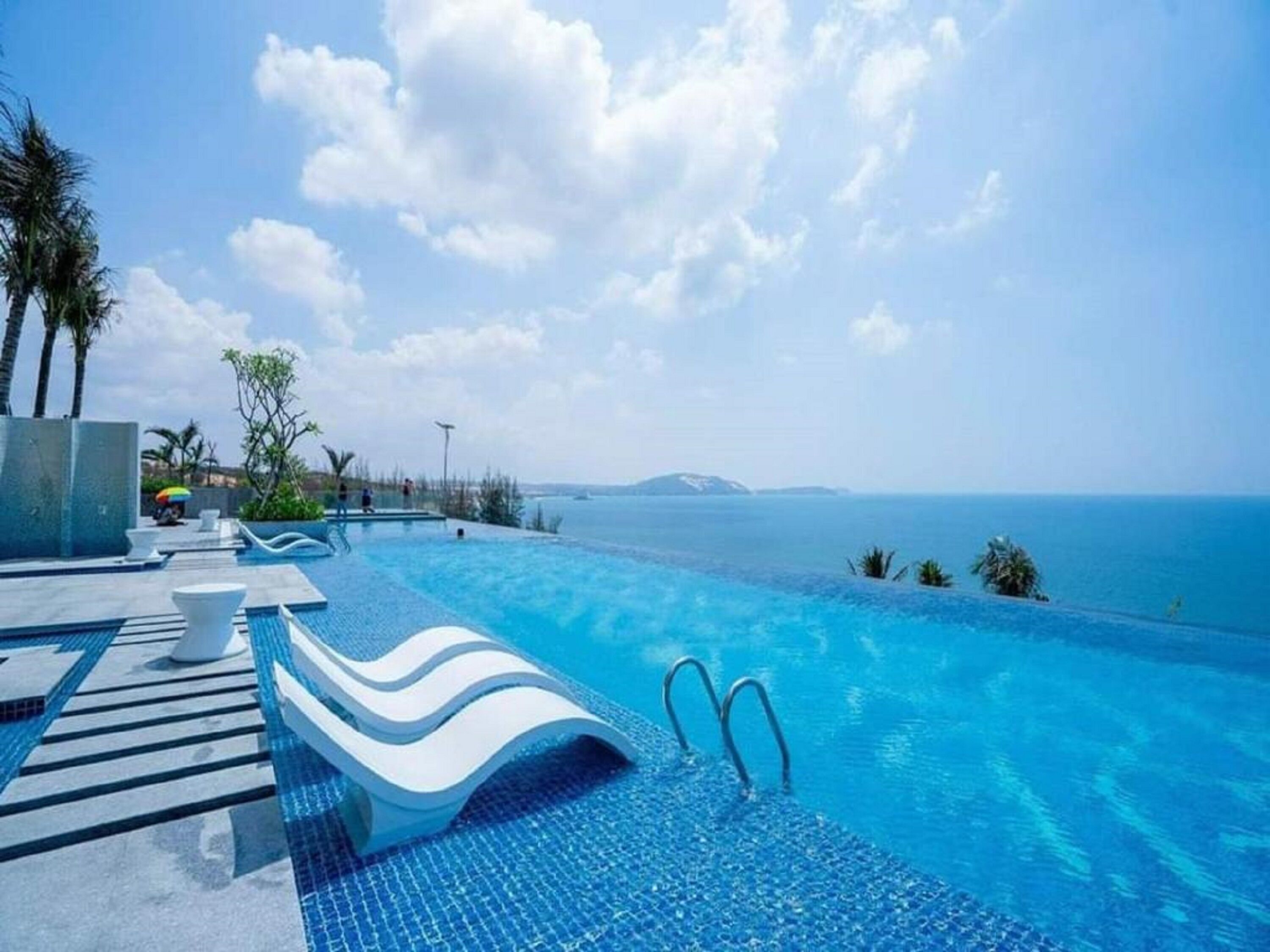 Une magnifique piscine à débordement d’un bleu profond, offrant une vue sur la mer et une île lointaine.