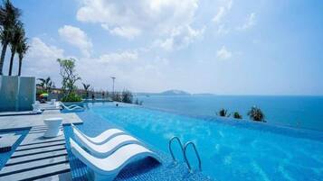 Une magnifique piscine à débordement d’un bleu profond, offrant une vue sur la mer et une île lointaine.