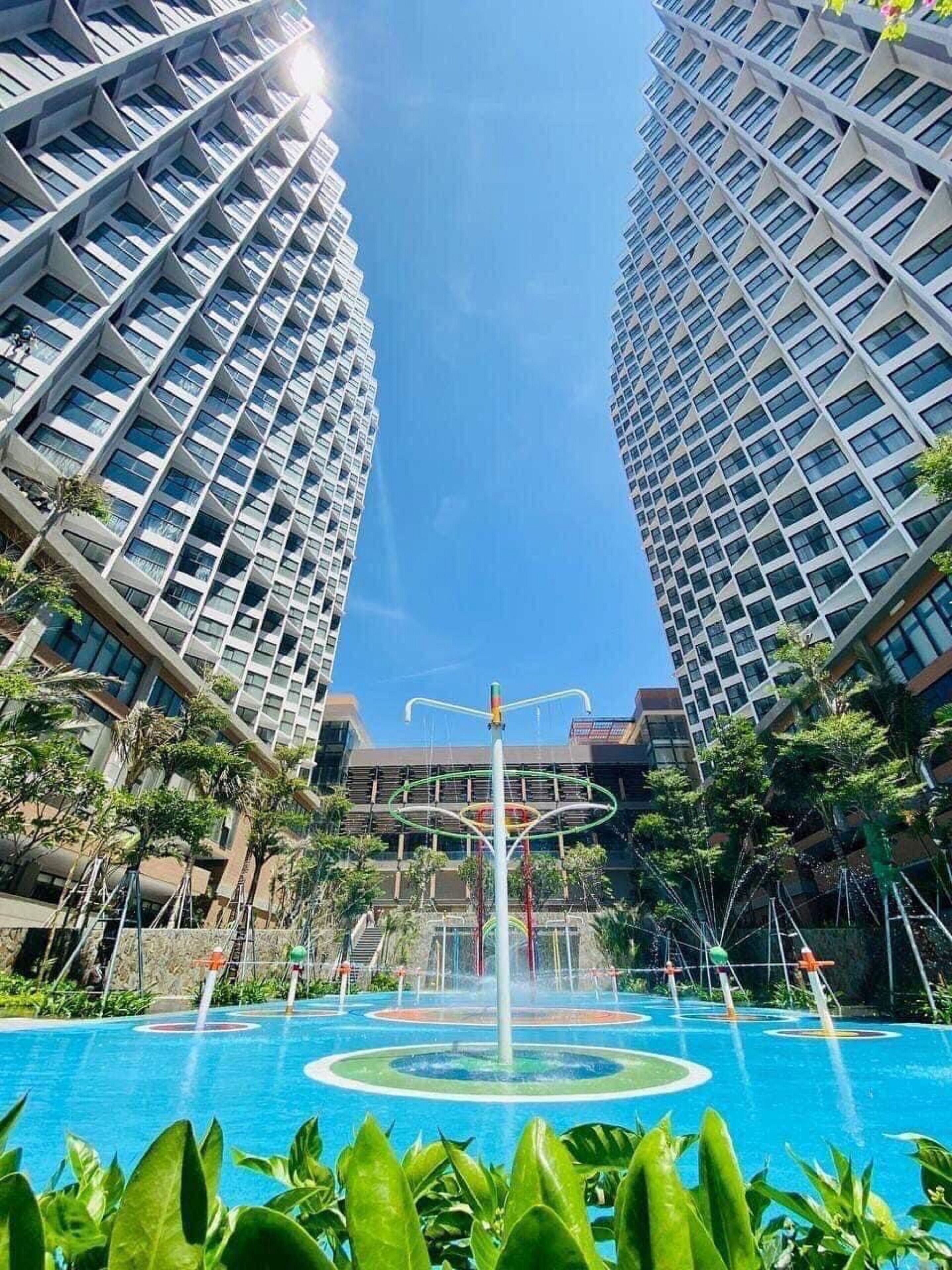 Un immeuble moderne de grande hauteur, doté d’un élément aquatique central et entouré de verdure.