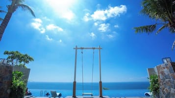 An infinity pool with a swing set and palm trees, overlooking the ocean.