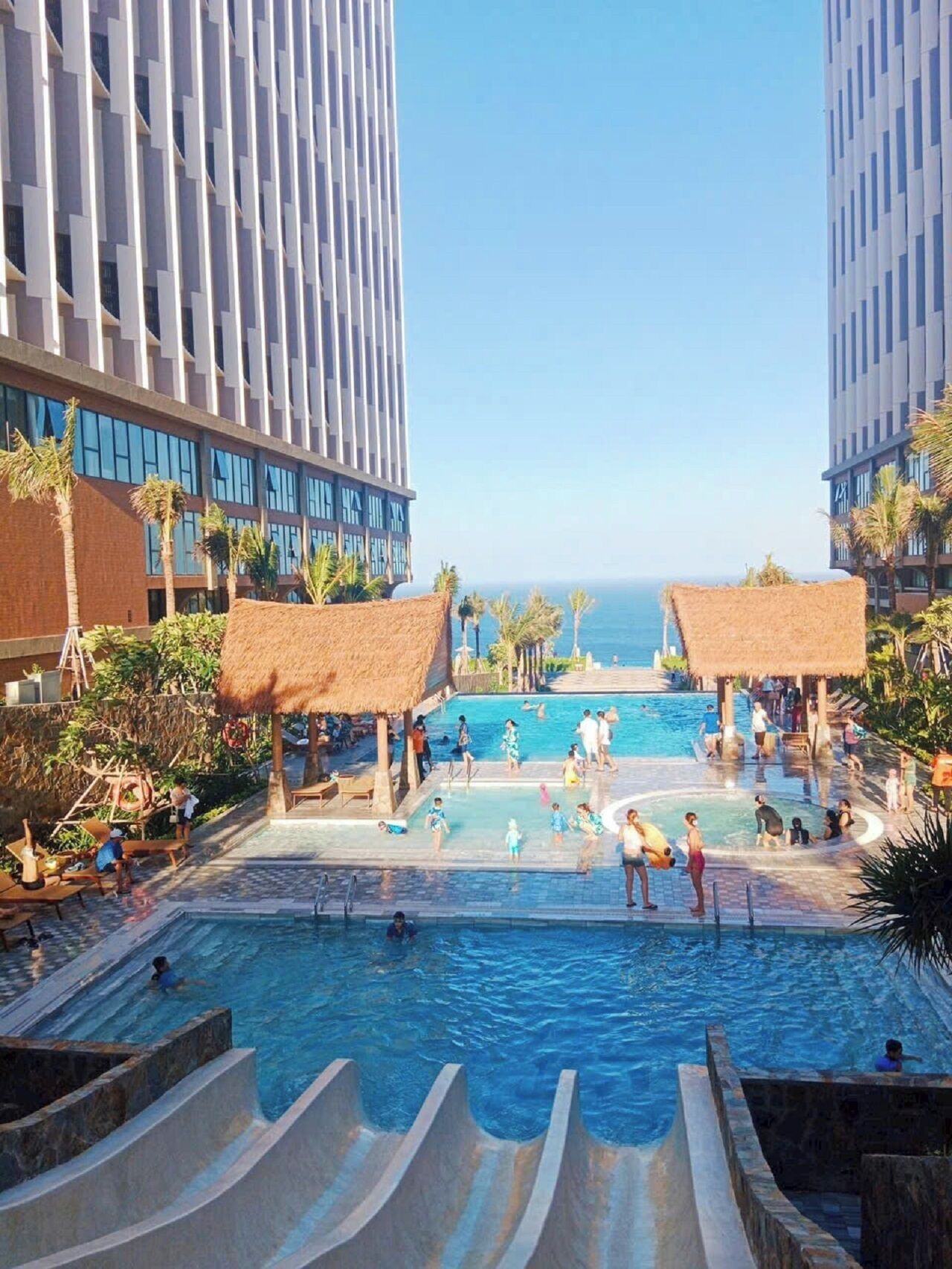 A resort pool area with multiple swimming pools, palm trees, and a view of the ocean.