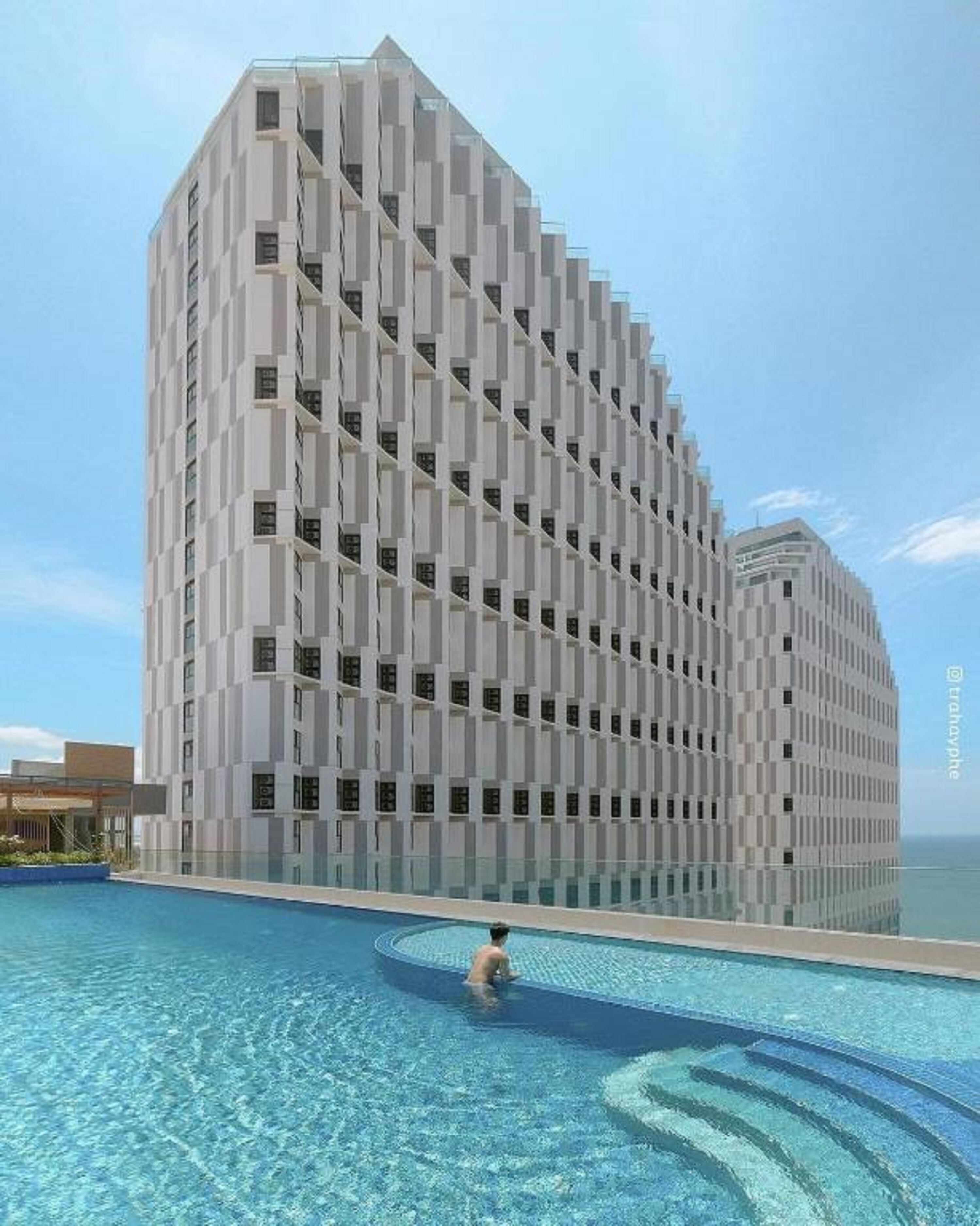 A modern hotel with a unique curved facade, a swimming pool, and a clear view of the sea.