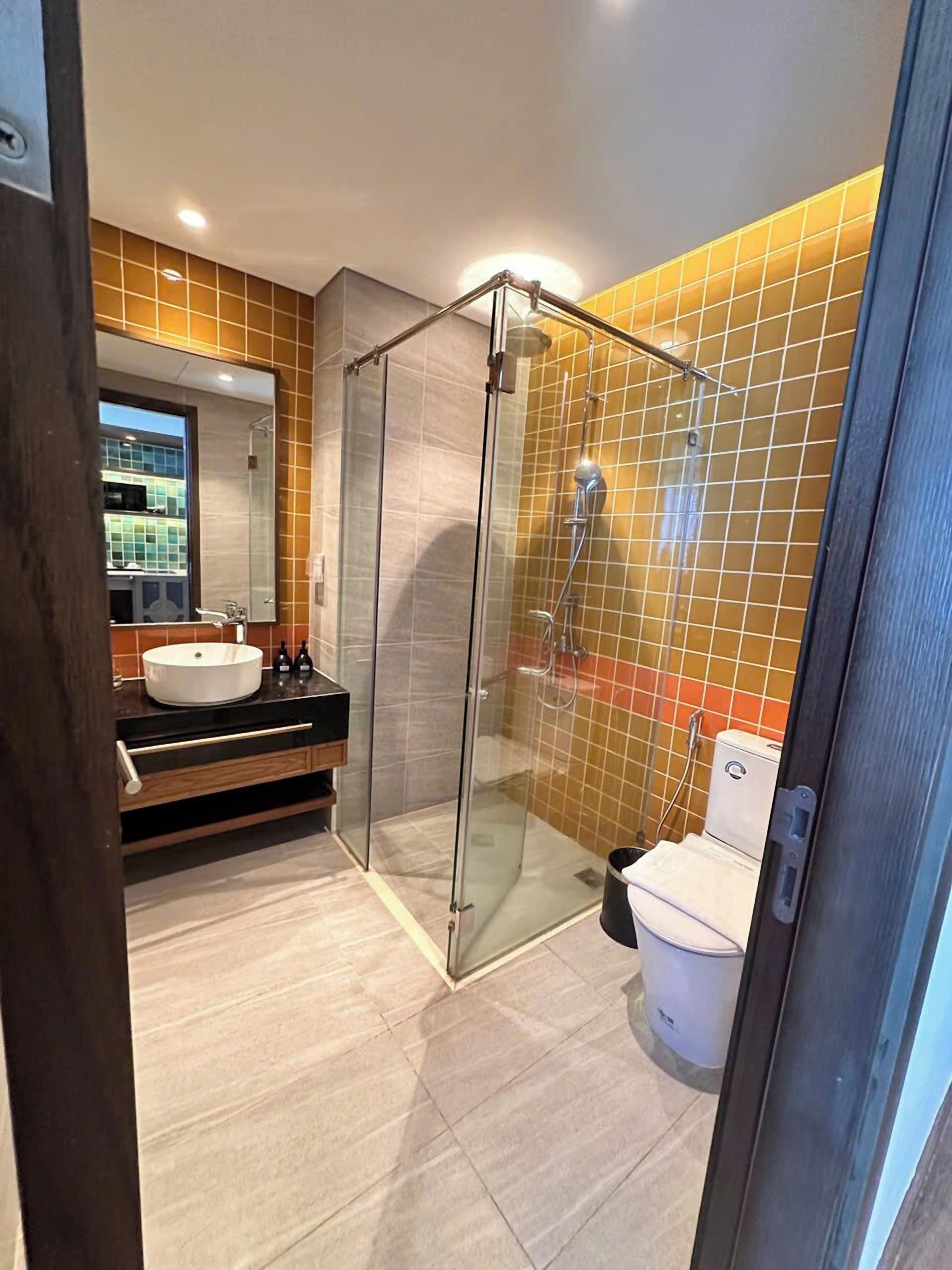 Un baño moderno con ducha de vidrio, lavabo redondo y un inodoro.