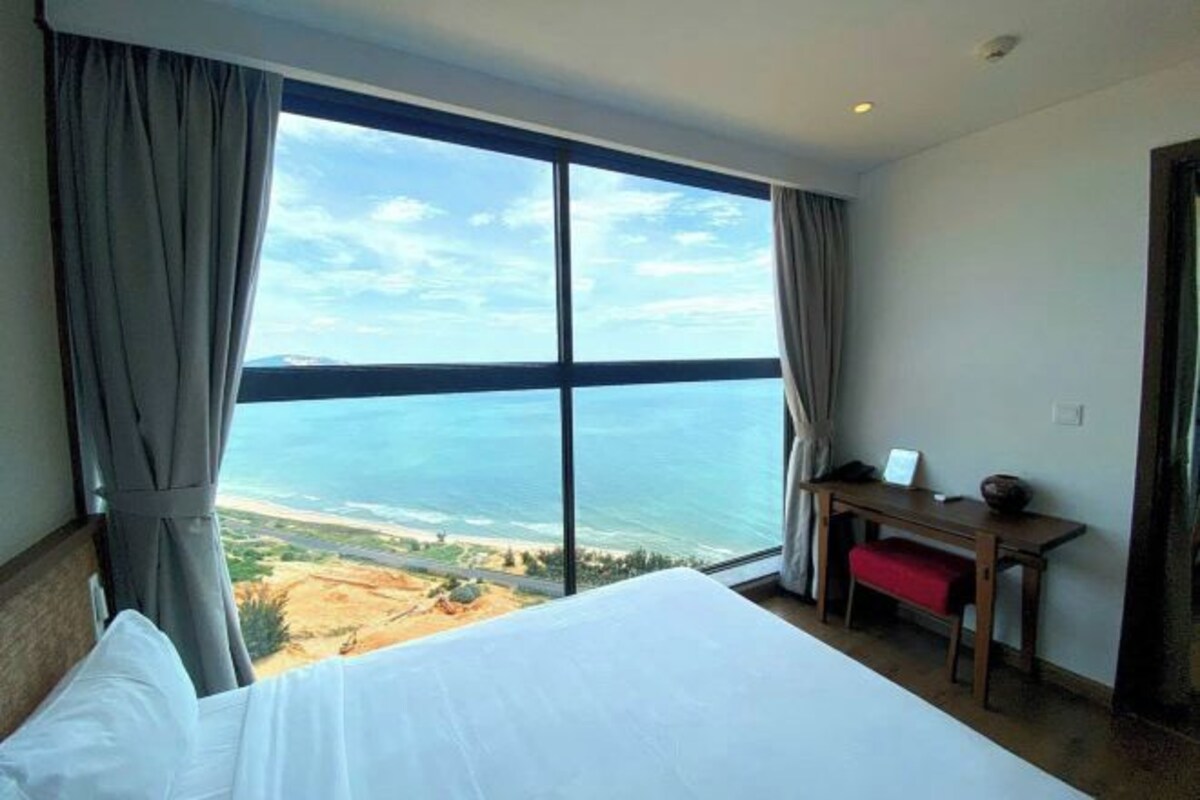 Een hotelkamer met een groot raam dat uitzicht biedt op het strand en de oceaan.