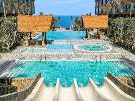 A resort pool area with a central pool, a smaller circular pool, and a water slide.