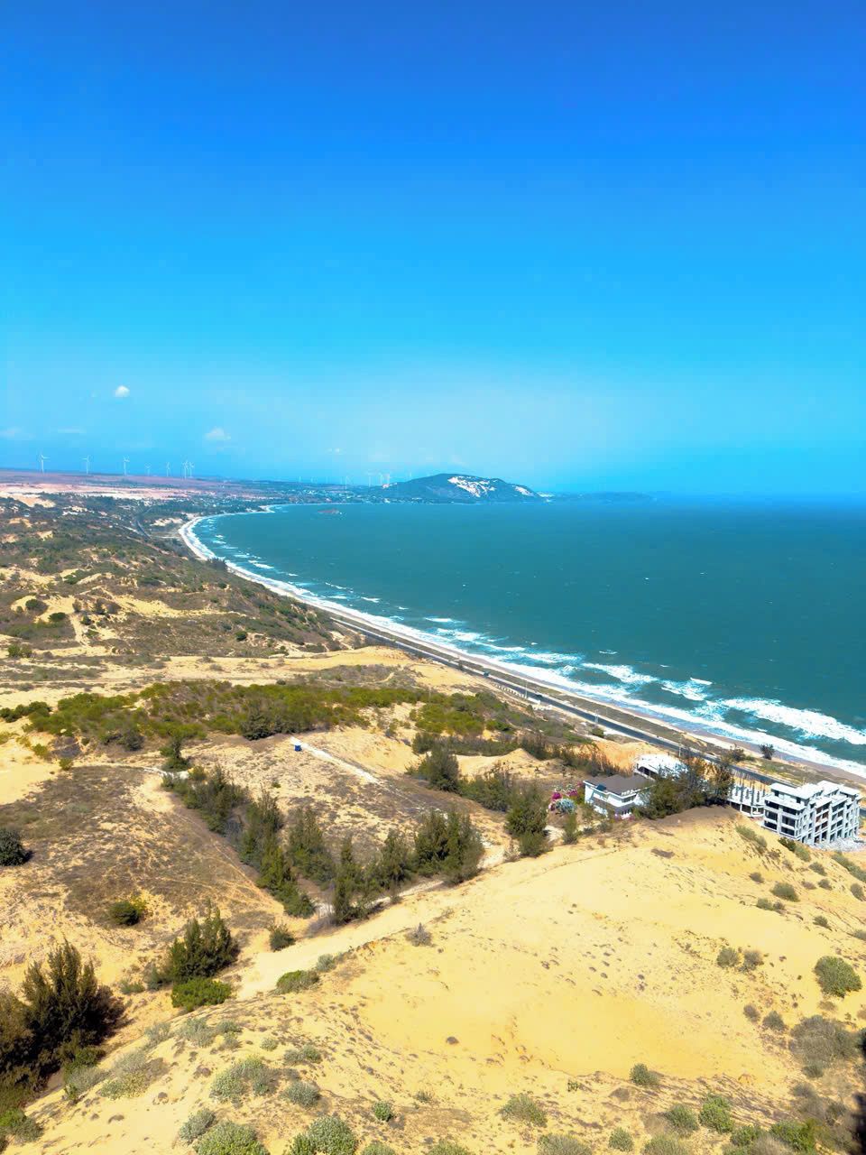 Un paisaje costero con playa, dunas y un edificio de varios pisos.