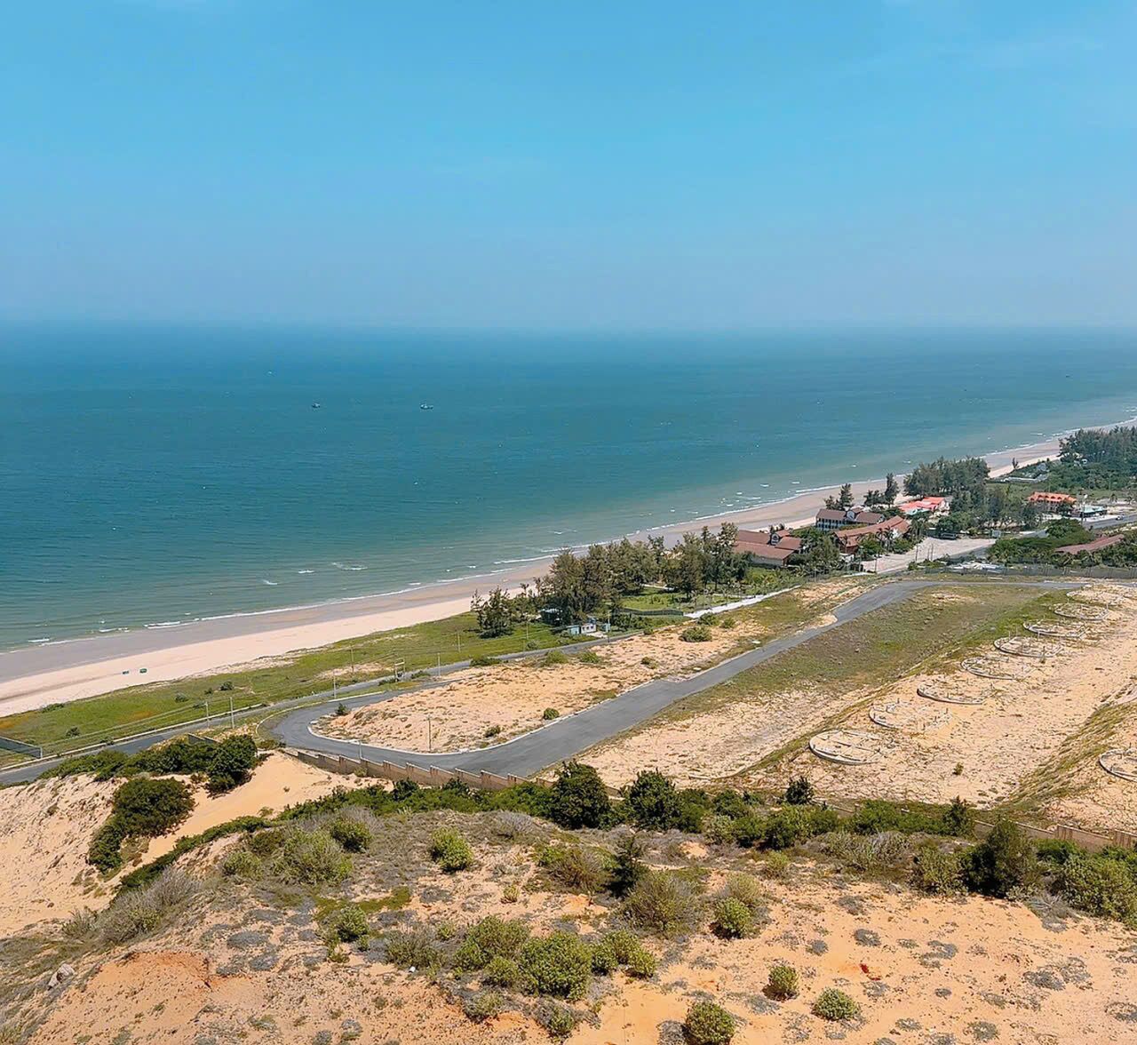 A coastal landscape with a beach, a road, and scattered buildings.