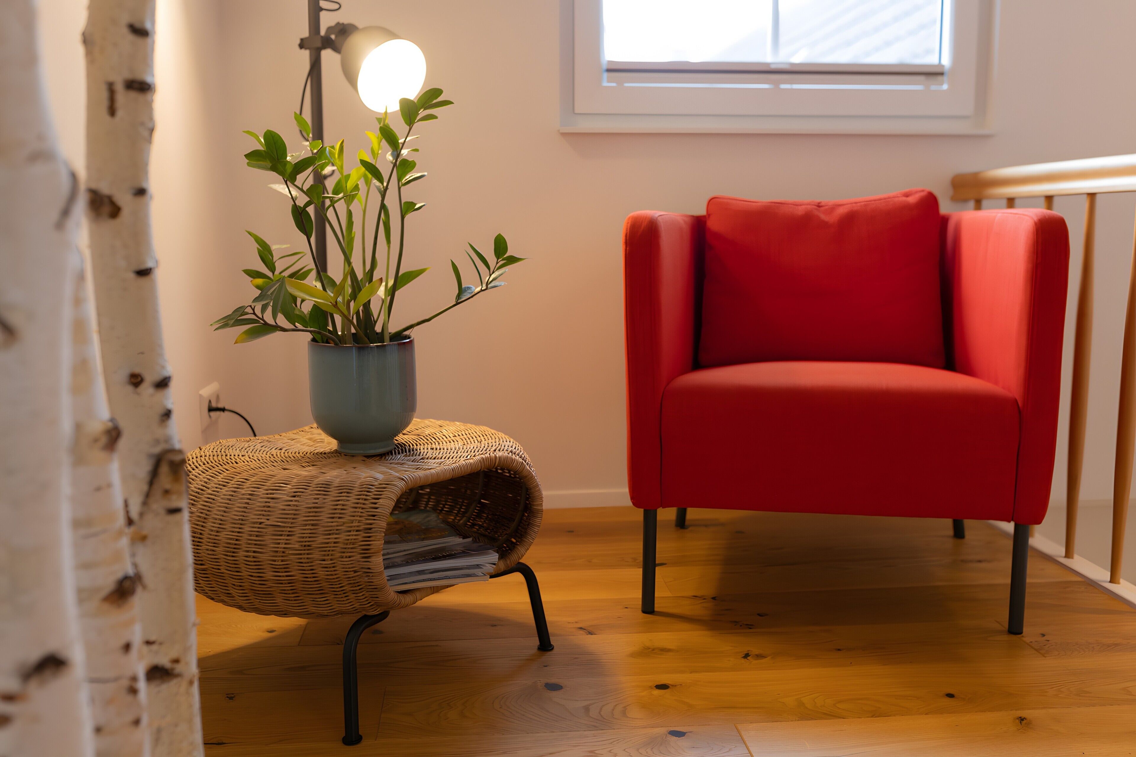 A red chair, a wicker side table with a lamp, and a potted plant.