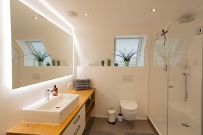 A modern bathroom with a large mirror, a sink, a toilet, and a shower.