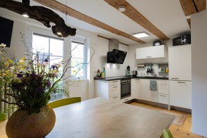 A modern kitchen with white cabinets, a wooden ceiling, a dining table, and a vase with flowers.