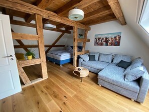 A room with a wooden ceiling, a grey sofa, a small round wicker table, and a painting on the wall.