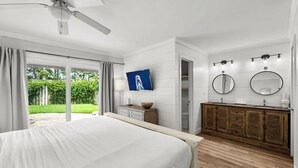 A bedroom with a bed, a ceiling fan, a TV, a wooden dresser, and a bathroom with two sinks and mirrors. - Brand New Golf Cart ~ Beach, Golf & Tennis (Miramar Beach)