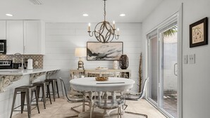 A modern kitchen with white cabinetry, a round glass-top table, and a chandelier. - Brand New Golf Cart ~ Beach, Golf & Tennis (Miramar Beach)