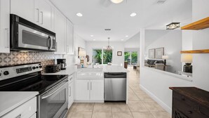 A modern kitchen with white cabinetry, stainless steel appliances, and a central island. - Brand New Golf Cart ~ Beach, Golf & Tennis (Miramar Beach)