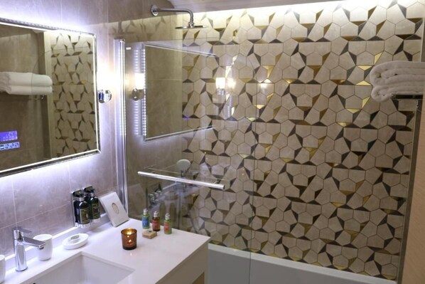 Un baño moderno con un salpicadero de azulejos geométricos, cabina de ducha de vidrio y tocador con artículos de aseo.
