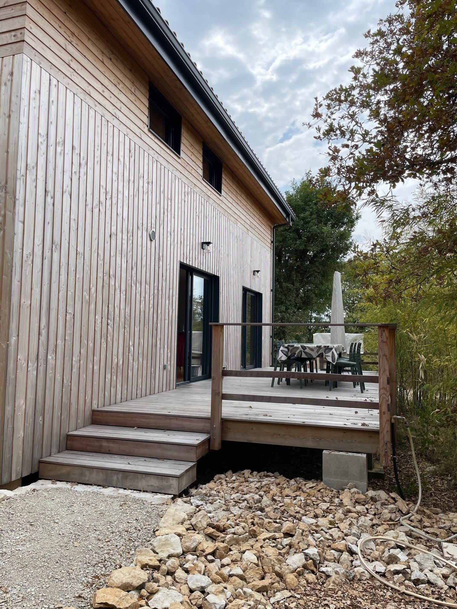 A modern building with a wooden exterior, a deck with outdoor furniture, and a stone monument.
