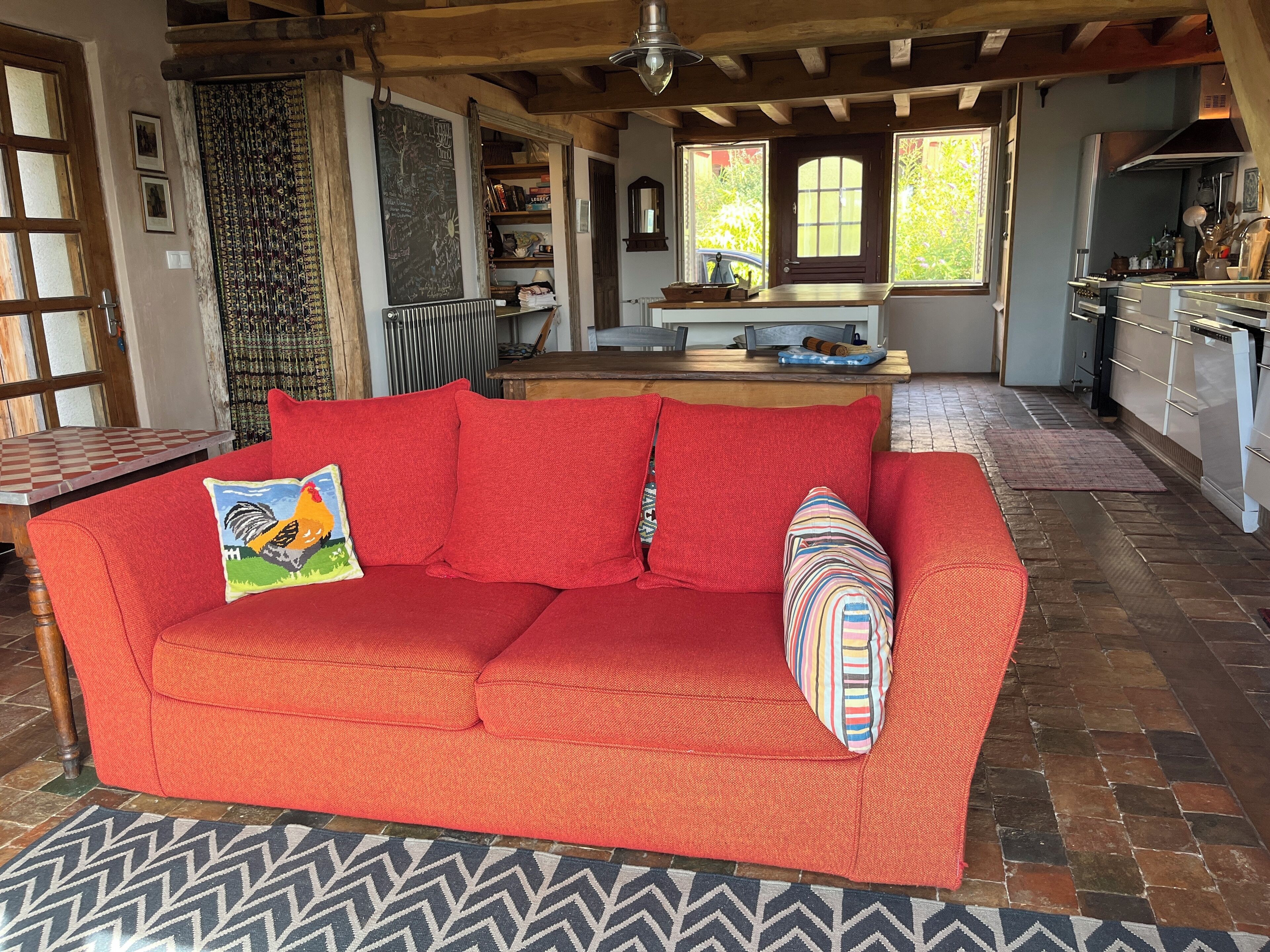 A cozy living room with a red sofa, a patterned rug, and a wooden ceiling.
