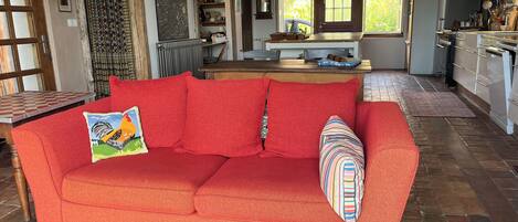 A cozy living room with a red sofa, a patterned rug, and a wooden ceiling.