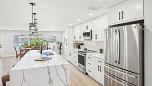 A modern kitchen with white cabinets, a large stainless steel refrigerator, and a marble island.