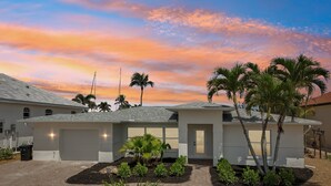 A modern house with a garage, surrounded by palm trees and a brick driveway.