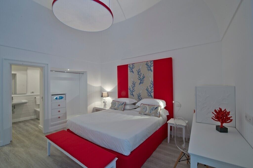Une chambre moderne avec un grand lit, des tables de chevet, un bureau et un mur d’accent rouge.