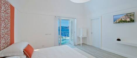 A modern hotel room with a large bed, a balcony with a view, and a painting on the wall.