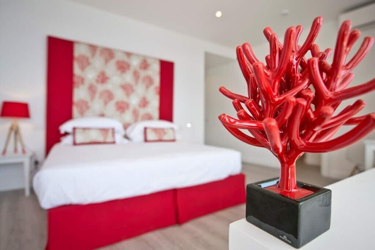 A modern bedroom with a bed, a red abstract sculpture, and a red and white patterned headboard.