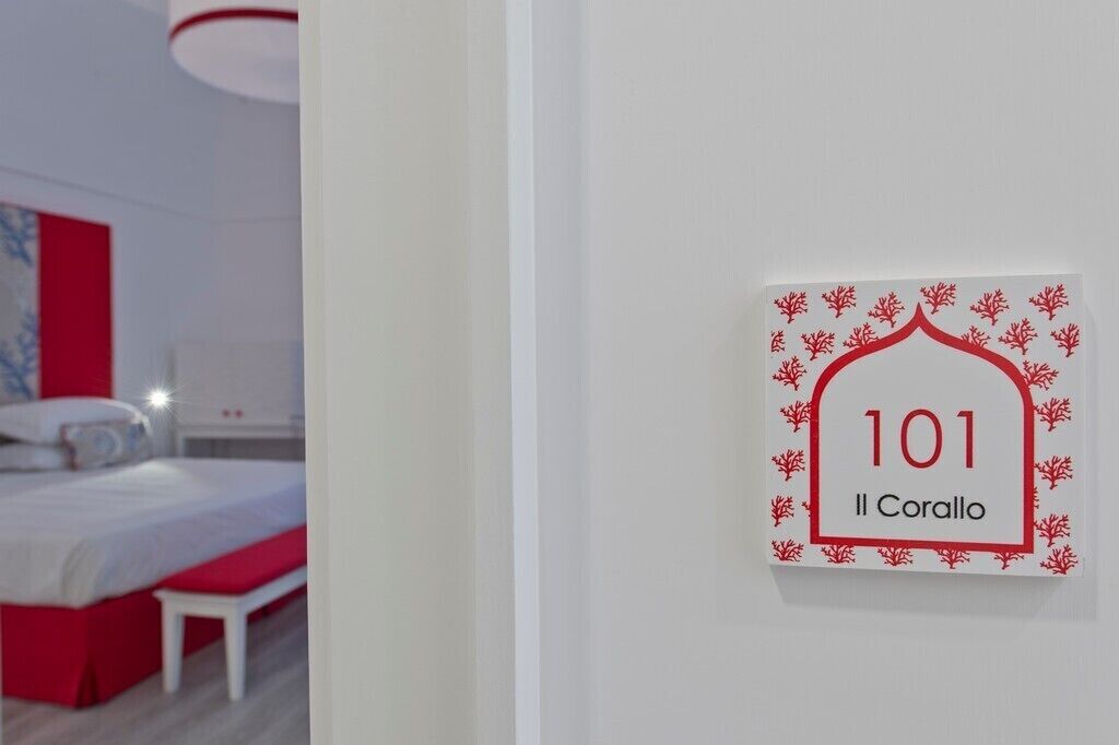 Habitación de hotel con cama, una banca y un letrero en la pared que indica el número 101.
