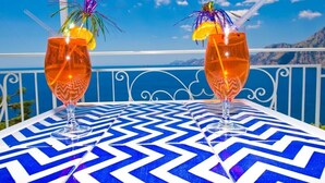 Two cocktail glasses on a table with a blue and white chevron pattern, set against a backdrop of a clear blue sky and distant mountains. - Il Corallo Praiano (Praiano)