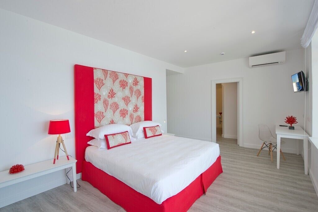A modern hotel room with a large bed, a bedside table with a lamp, a small desk, and an air conditioning unit on the wall.