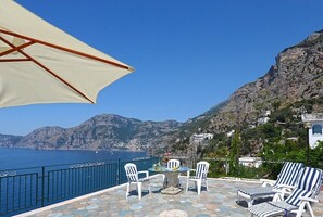 A terrace with a table and chairs, overlooking a mountainous coastline. - Il Corallo Praiano (Praiano)