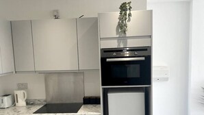 Moderni keittiö, jossa on valkoiset kaapit, sisäänrakennettu uuni, jääkaappi ja marmorinen työtaso.