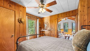 Ein Schlafzimmer einer Holzhütte mit einem Bett, einem Deckenventilator und Blick ins Freie.