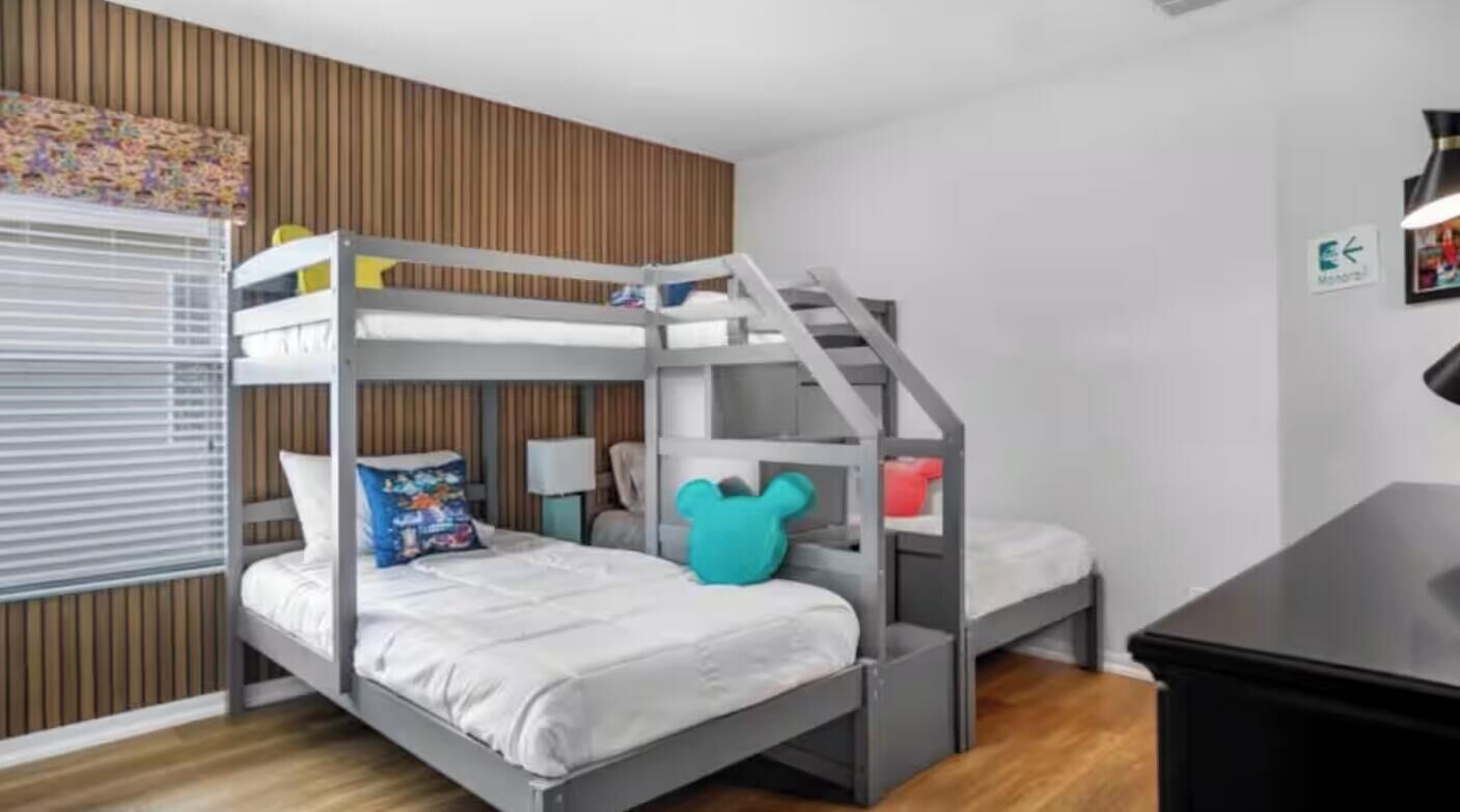 A bunk bed room with a wooden slat wall, a desk, and a window with blinds.