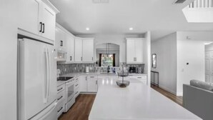 Una cocina moderna con armarios blancos, una isla central y un rincón comedor con un sofá gris.