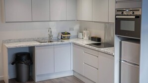 A modern kitchen with white cabinets, a marble countertop, a sink, a kettle, and a built-in oven.