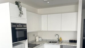 A compact kitchen with white cabinets, a built-in oven, a sink, and a trash bin.