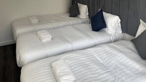 A hotel room with three beds, each with white linens and pillows, a grey headboard, and a pendant light.